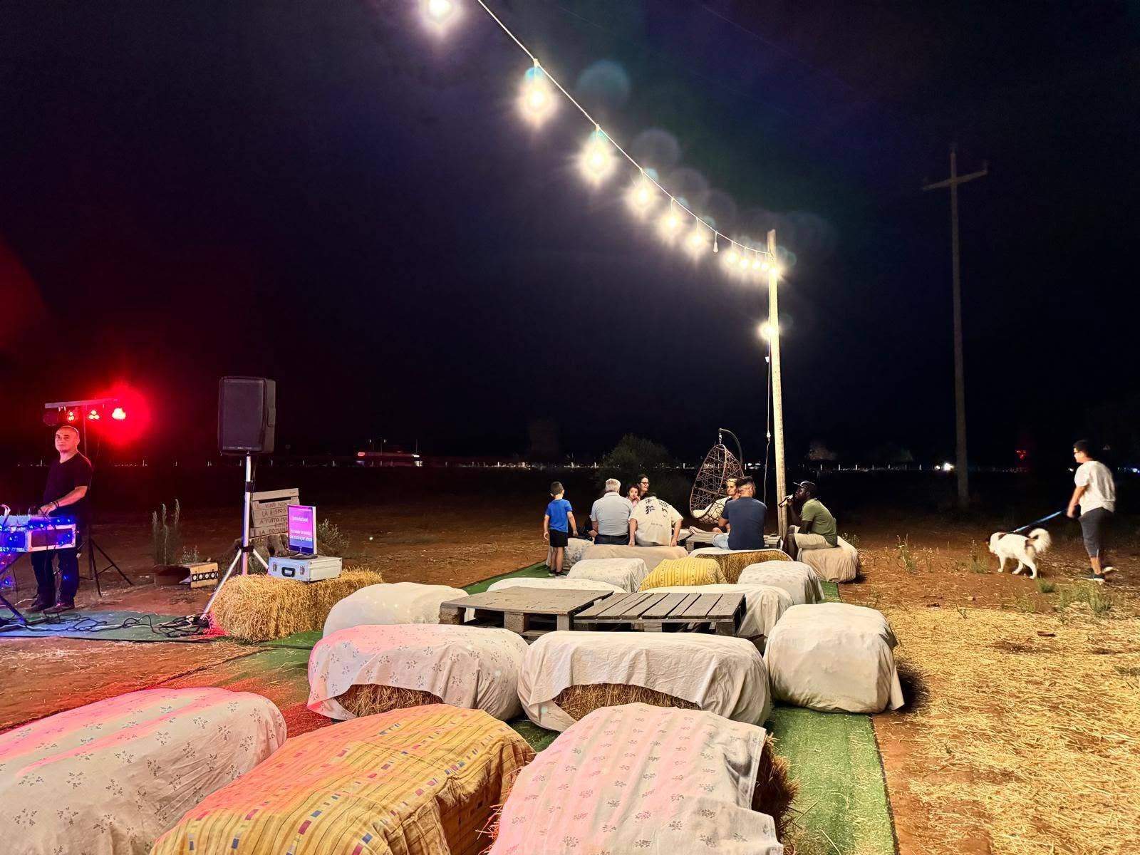 Serata all'aperto di Agrifood da Francesco: balle di fieno con teli, tavolini di pallet, luci sospese e console dj